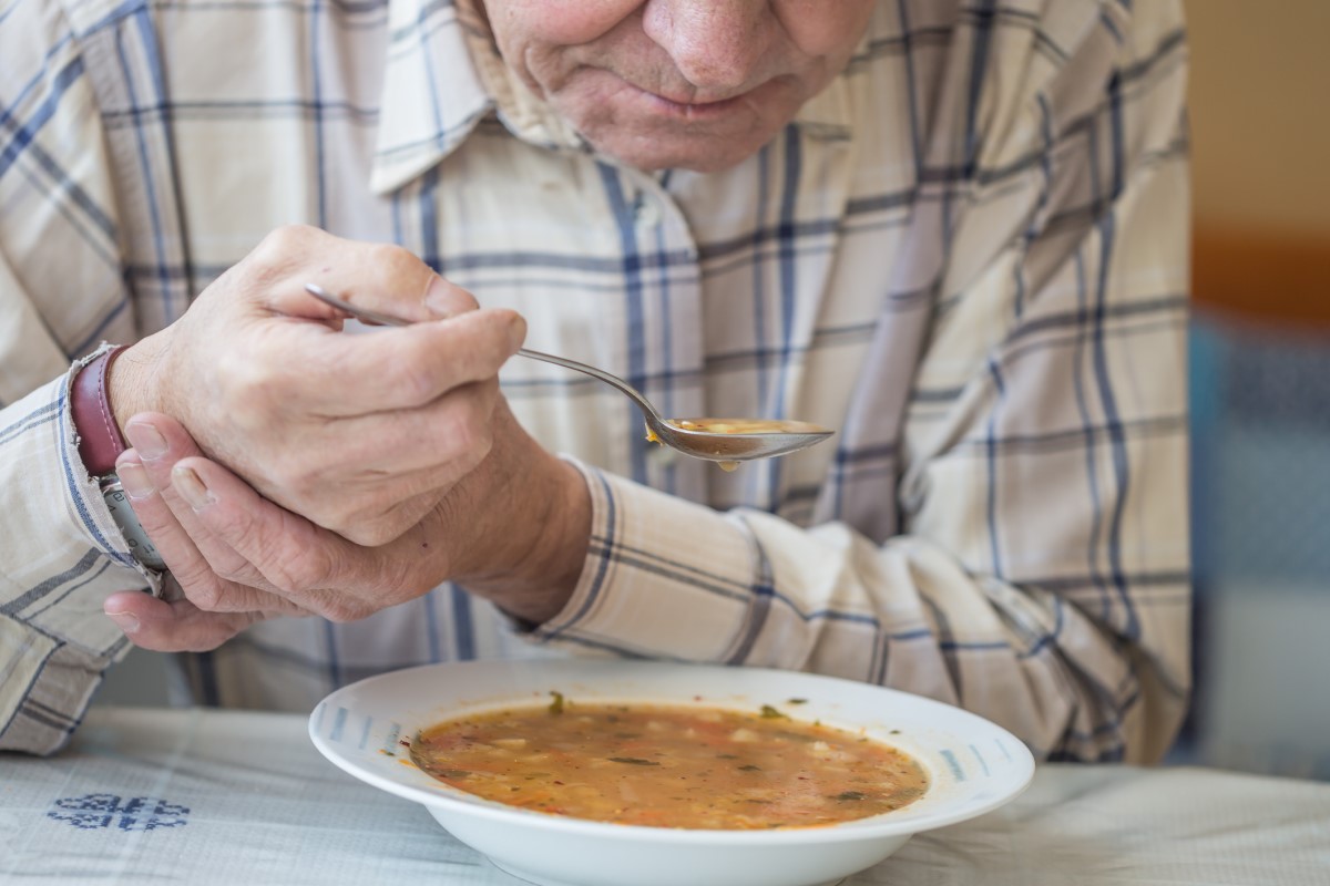 Parkinson hastalığında titremeye karşı çorba içip elini tutan adam