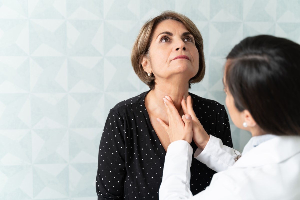 Tiroid bezini palpe eden doktor, karşısında oturan yaşlı kadın