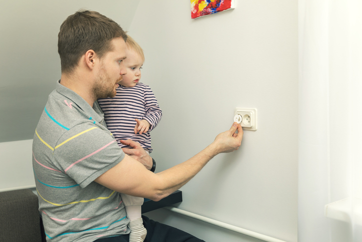 Baba küçük bir çocuğu kucağında tutar ve elektrik fişiyle fişi kapatır