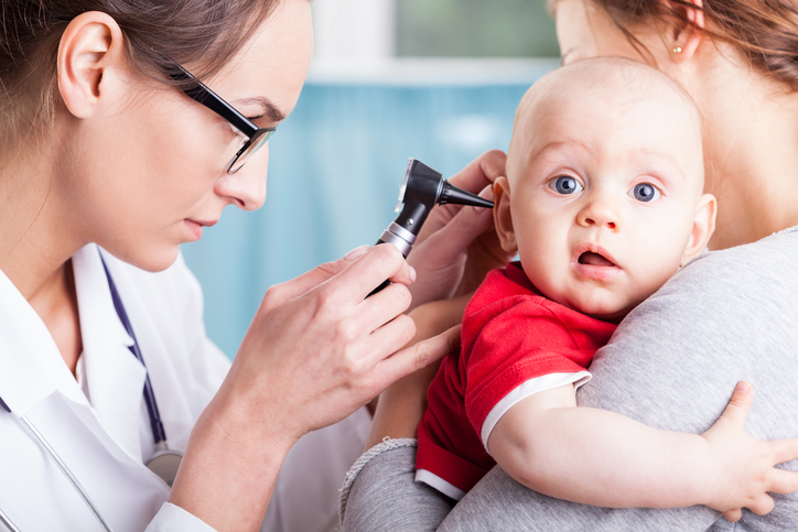 bir doktor bir çocuğun kulağını bir makine ile muayene eder