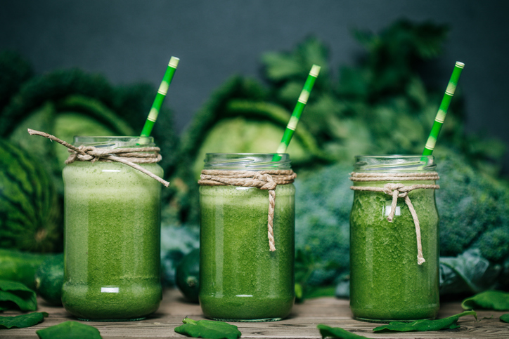 Yeşil sebzeli smoothie, üç bardak, arka planda lahana, brokoli ve bezelye