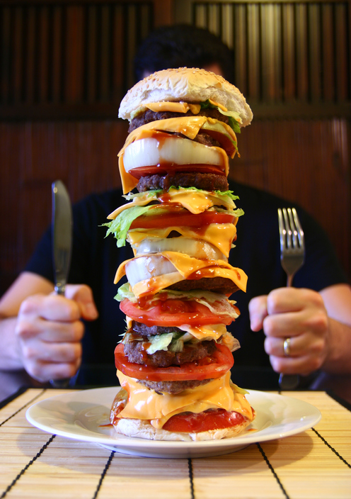 Tabağında uzun bir hamburger olan bir adam masada oturuyor.